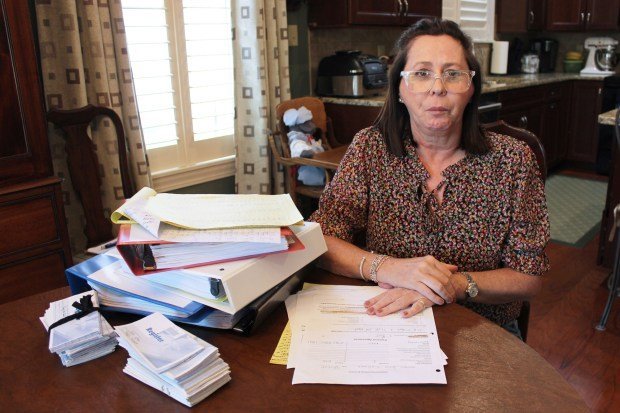 A woman sits at a table stacked with paperwork