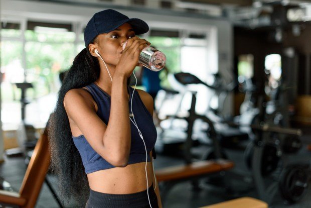 Sade su artık yok. Hidrasyon takviyeleri artık var. Peki bu en iyi 8 marka gerçekten işe yarıyor mu? 1 A woman wearing headphones and a hat drinks water at a gym