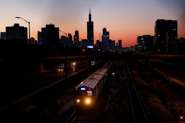 A CTA Blue Line train heads west as the sun rises behind the Chicago skyline on July 7, 2024. (Armando L. Sanchez/Chicago Tribune)