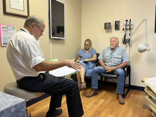 Fred Hardwicke, an oncologist, reviews medical notes with Dennis and Mary Ellen Woodward. Dennis has a type of non-Hodgkin lymphoma. (Charlotte Huff/KFF Health News/TNS)