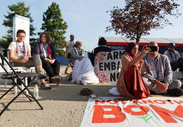 Uncommitted delegates sit on the ground Asma Nizami, left, and Abbas Alawieh, right, participate an interview on their phone with national media while during a sit-in in front of the United Center on Aug. 22. 2024, in Chicago. (Stacey Wescott/Chicago Tribune)