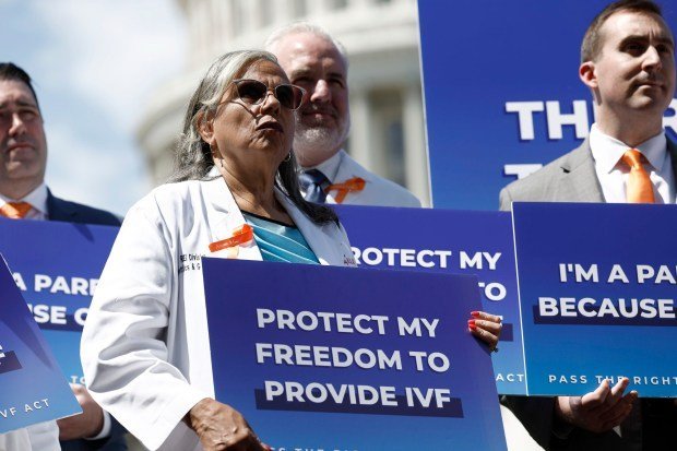 Protesters in medical coats hold blue signs that say "Protect My Freedom To Provide IVF"